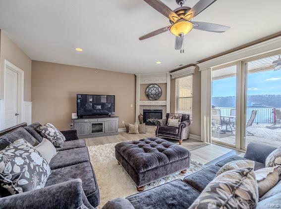 living area with light wood-style flooring, a large fireplace, and ceiling fan