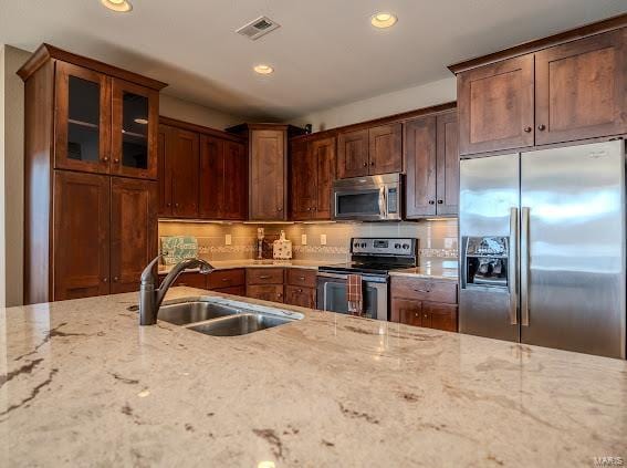 kitchen with stainless steel appliances, a sink, light stone countertops, recessed lighting, and glass insert cabinets