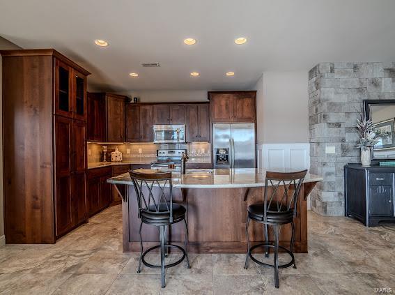 kitchen with appliances with stainless steel finishes, a breakfast bar, recessed lighting, a center island with sink, and glass insert cabinets