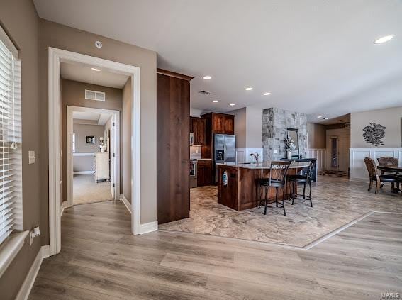 kitchen featuring a kitchen breakfast bar, light wood-type flooring, stainless steel fridge with ice dispenser, an island with sink, and recessed lighting