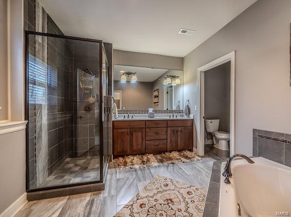 full bath featuring a stall shower, a bath, toilet, double vanity, and baseboards