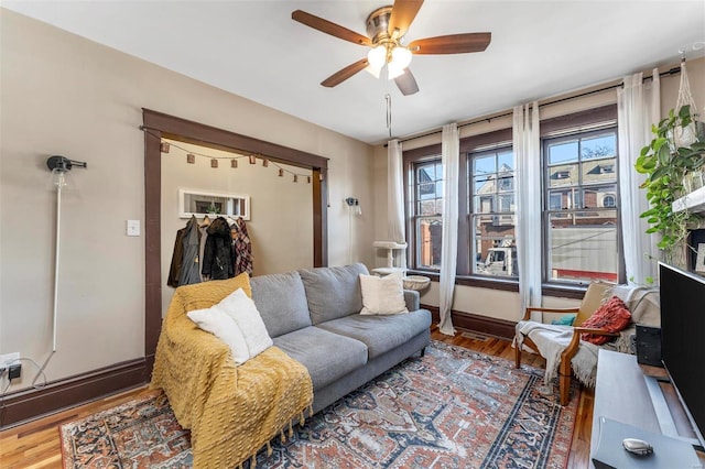 living area with a ceiling fan, wood finished floors, and baseboards