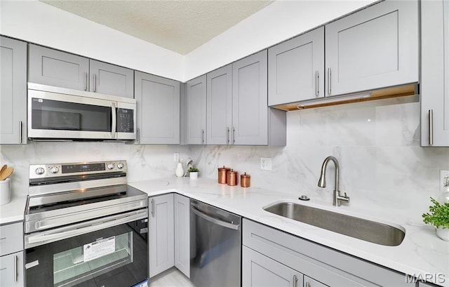 kitchen featuring appliances with stainless steel finishes, gray cabinets, a sink, decorative backsplash, and a textured ceiling