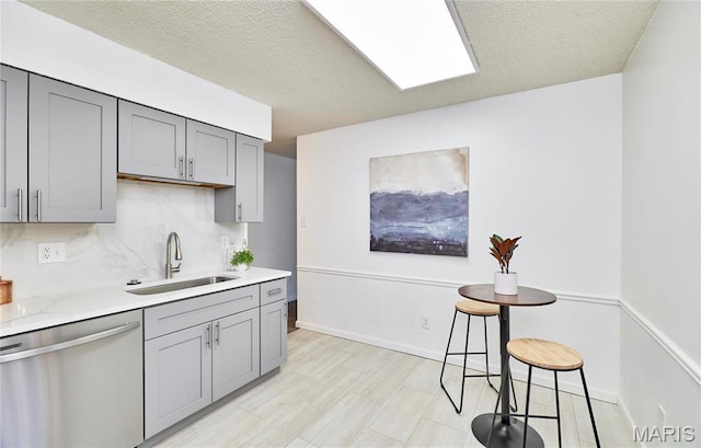 kitchen with stainless steel dishwasher, gray cabinetry, a sink, decorative backsplash, and baseboards