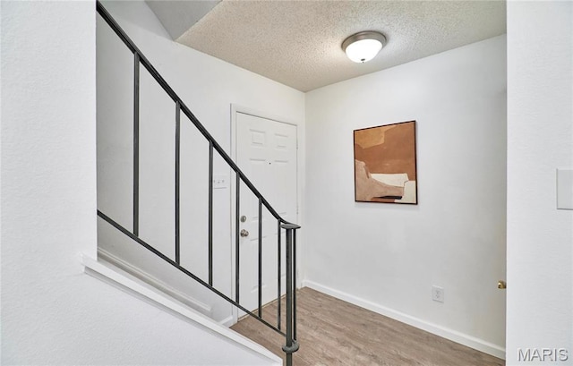 stairs with wood finished floors, a textured ceiling, and baseboards