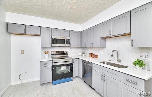 kitchen with appliances with stainless steel finishes, a sink, gray cabinetry, light countertops, and a textured ceiling