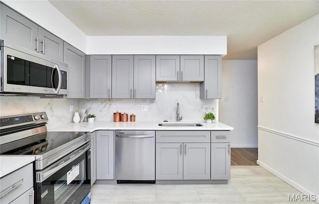 kitchen featuring appliances with stainless steel finishes, gray cabinetry, a sink, light countertops, and decorative backsplash
