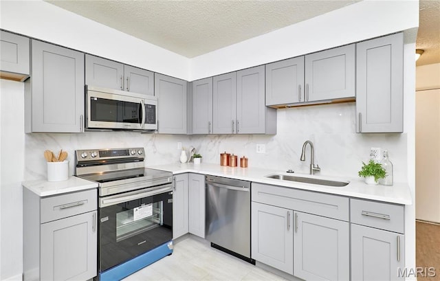 kitchen featuring stainless steel appliances, gray cabinets, a sink, and a textured ceiling