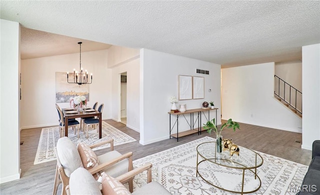 living area with a chandelier, a textured ceiling, wood finished floors, stairway, and baseboards
