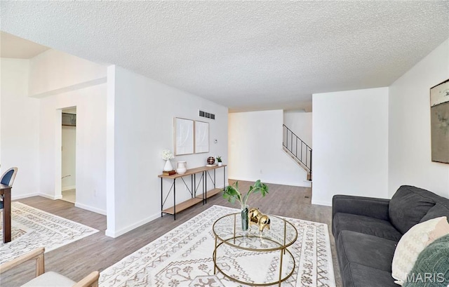 living room featuring stairway, wood finished floors, a textured ceiling, and baseboards