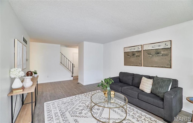 living area with stairs, wood finished floors, a textured ceiling, and baseboards