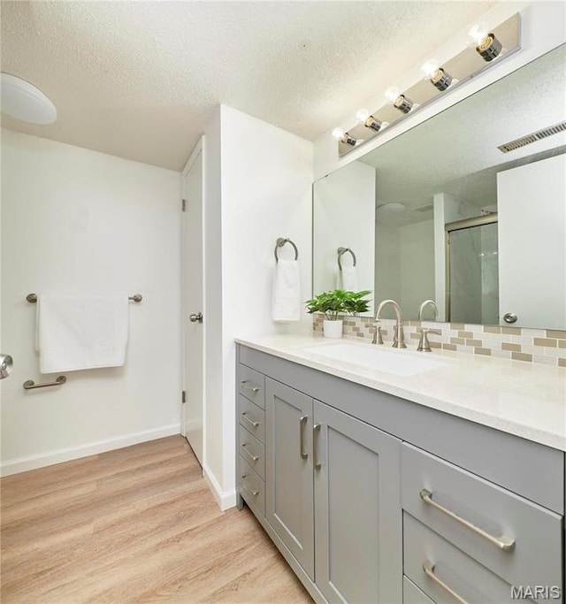 full bath featuring wood finished floors, a textured ceiling, vanity, a shower stall, and baseboards