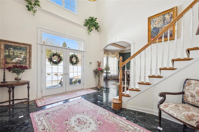 foyer entrance with a towering ceiling, marble tiled floors, arched walkways, healthy amount of natural light, and baseboards