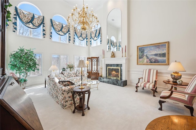 carpeted living area with a chandelier, a premium fireplace, a towering ceiling, a wainscoted wall, and a decorative wall
