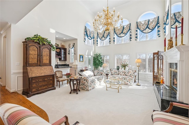 living room with crown molding, a chandelier, carpet, wainscoting, and healthy amount of natural light