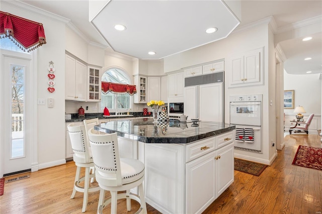 kitchen featuring oven, light wood-type flooring, glass insert cabinets, white cabinetry, and ornamental molding