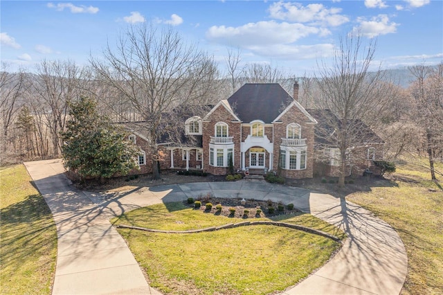 georgian-style home with a chimney, brick siding, a front yard, and curved driveway
