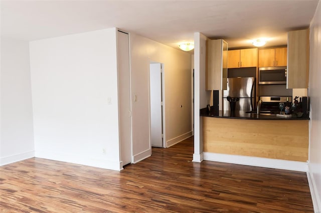 kitchen with appliances with stainless steel finishes, dark wood finished floors, light brown cabinetry, dark countertops, and baseboards