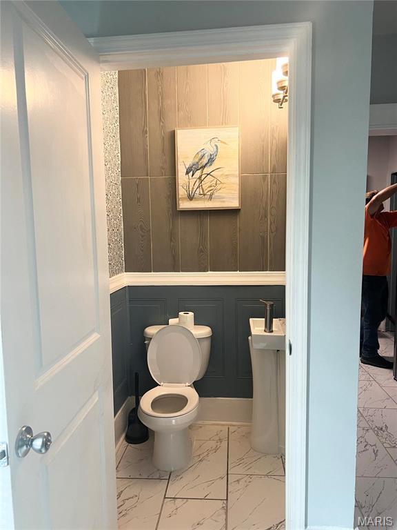3511 Oakdale Ave, Saint Louis, MO 63121 - bathroom featuring marble look tile flooring, toilet, and a wainscoted wall