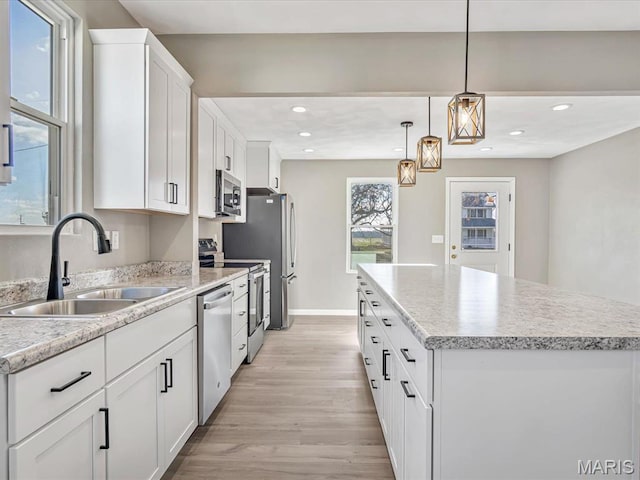 kitchen featuring a sink, appliances with stainless steel finishes, a center island, light wood-style flooring, and white cabinetry
