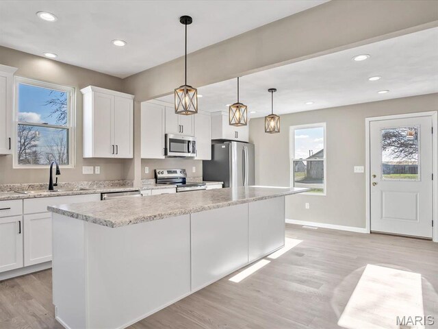 kitchen with stainless steel appliances, a sink, light wood-type flooring, a center island, and white cabinets