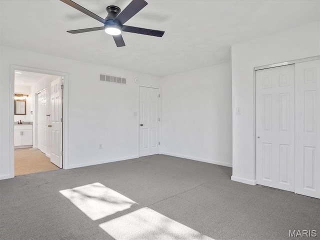 unfurnished bedroom featuring carpet, baseboards, ensuite bath, a closet, and ceiling fan