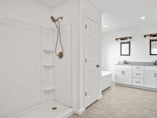 bathroom with a stall shower, double vanity, baseboards, and recessed lighting