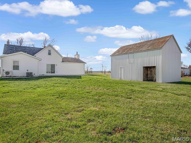 view of grassy yard with an outdoor structure, central air condition unit, and a pole building