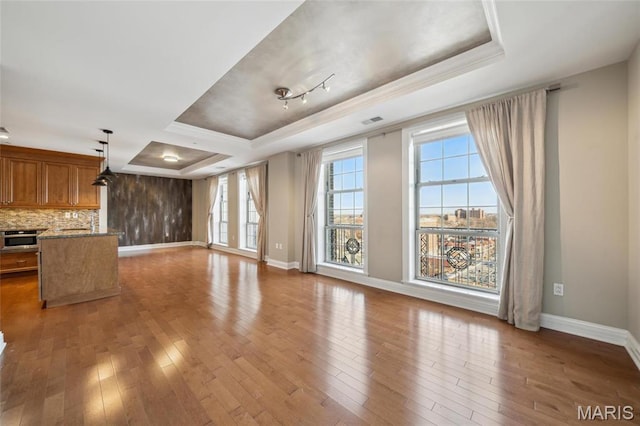 unfurnished living room featuring a raised ceiling, healthy amount of natural light, hardwood / wood-style floors, and ornamental molding