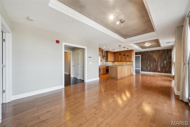 unfurnished living room featuring a tray ceiling, baseboards, wood finished floors, and ornamental molding