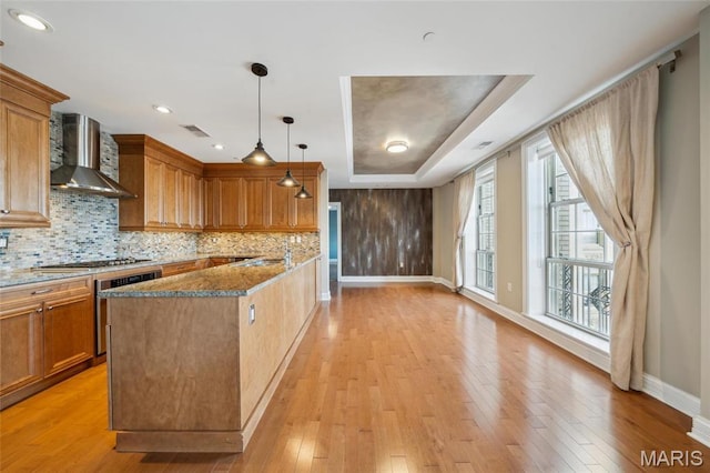 kitchen featuring wall chimney exhaust hood, baseboards, wall oven, stainless steel gas cooktop, and tasteful backsplash