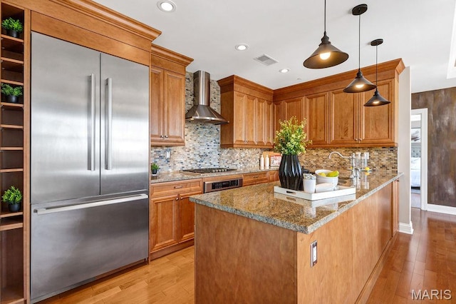 232 N Kingshighway Blvd Unit 1201, Saint Louis, MO 63108 - kitchen featuring appliances with stainless steel finishes, wall chimney exhaust hood, light wood finished floors, brown cabinetry, and stone countertops