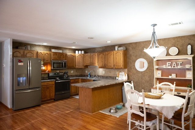 12332 Triple E Ln, Berger, MO 63014 - kitchen featuring appliances with stainless steel finishes, a peninsula, brown cabinetry, wood finished floors, and hanging light fixtures