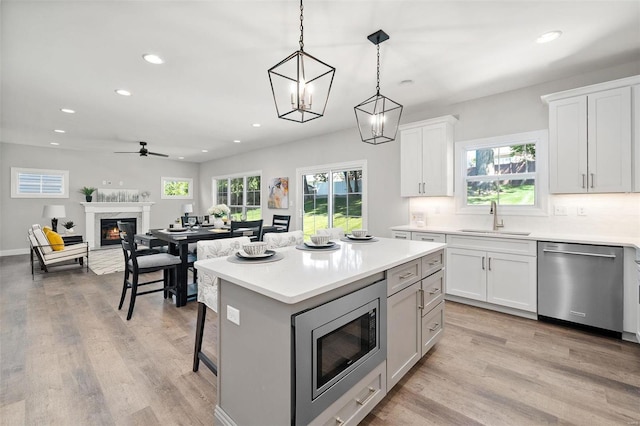 kitchen featuring appliances with stainless steel finishes, a sink, recessed lighting, a fireplace, and light wood-style floors