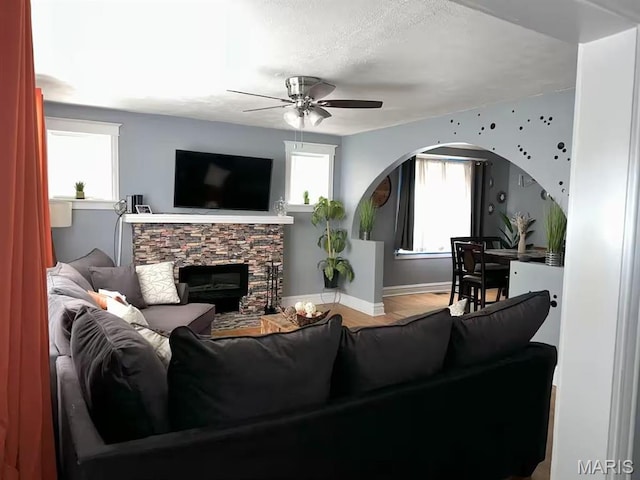 4983 Chippewa St, Saint Louis, MO 63109 - living room featuring ceiling fan, a stone fireplace, baseboards, wood finished floors, and arched walkways