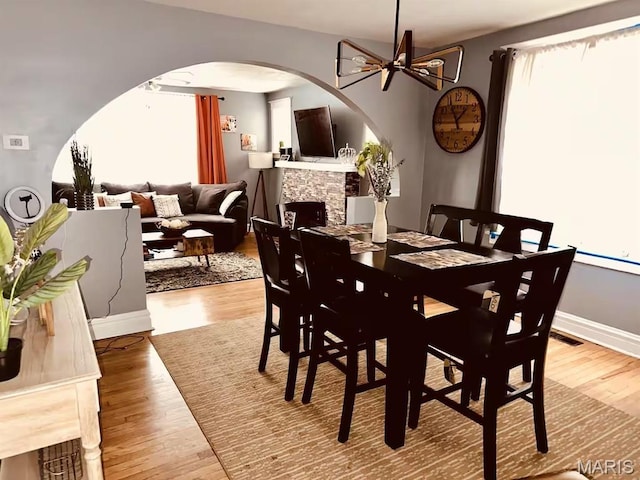 4983 Chippewa St, Saint Louis, MO 63109 - dining room featuring arched walkways, wood finished floors, a stone fireplace, baseboards, and a chandelier