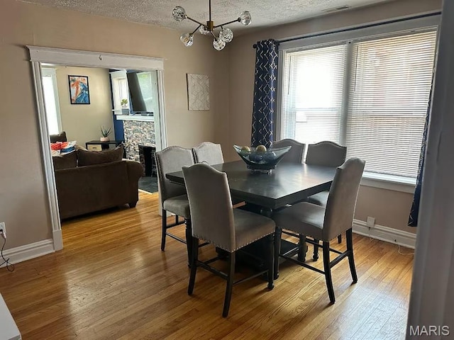 4983 Chippewa St, Saint Louis, MO 63109 - dining room featuring light wood-type flooring, a textured ceiling, baseboards, a stone fireplace, and a chandelier
