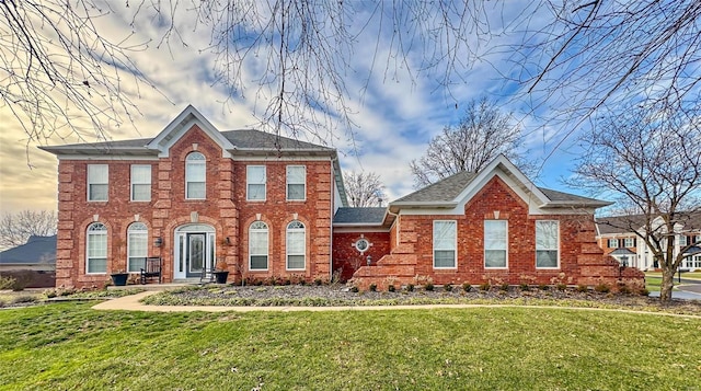 colonial home with brick siding, a front yard, and a shingled roof