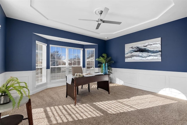 office area featuring carpet flooring, ceiling fan, a wainscoted wall, and a raised ceiling