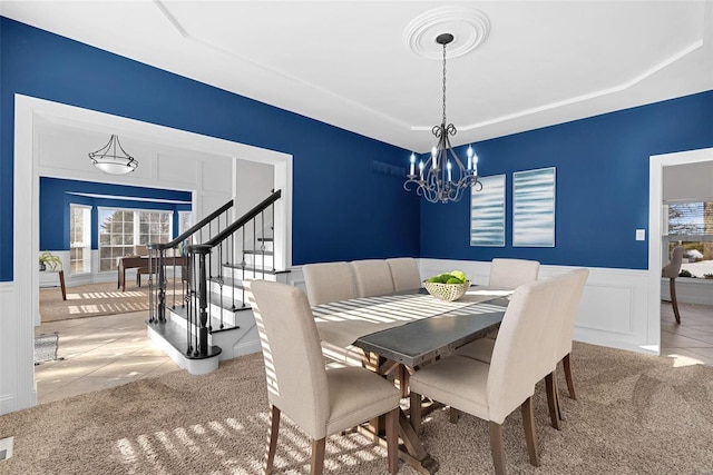 carpeted dining room with stairs, a chandelier, a wainscoted wall, a decorative wall, and a tray ceiling
