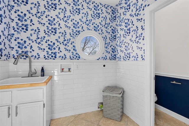 bathroom featuring wainscoting, wallpapered walls, tile walls, tile patterned flooring, and toilet