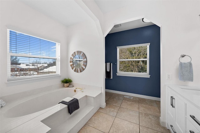 bathroom featuring healthy amount of natural light, tile patterned flooring, a garden tub, and baseboards