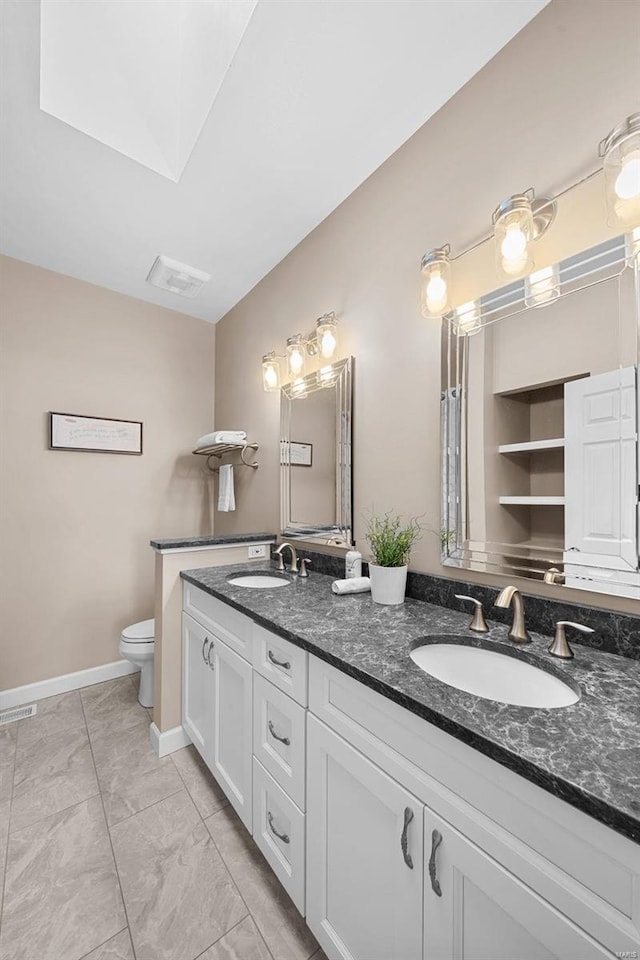 bathroom featuring toilet, double vanity, baseboards, and marble look tiles
