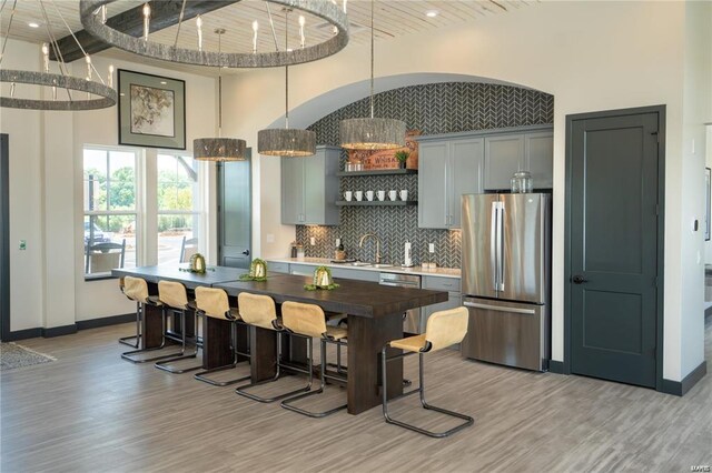 103 Cardow Dr Unit 169-605, Ofallon, MO 63368 - kitchen featuring stainless steel appliances, light wood-style floors, baseboards, tasteful backsplash, and a towering ceiling