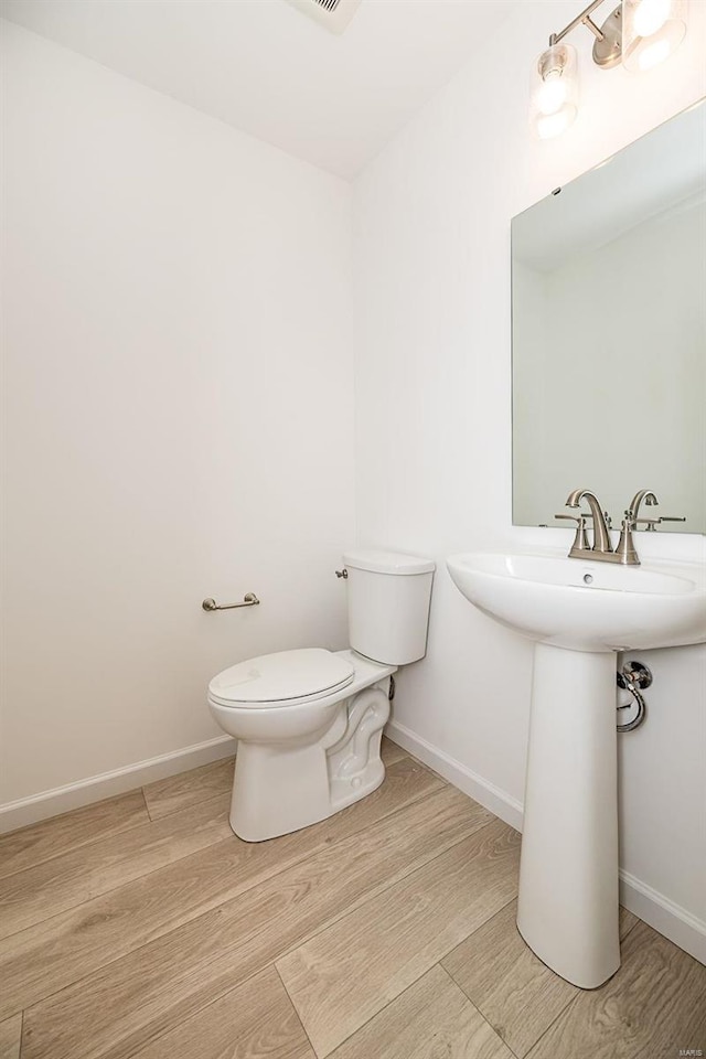 bathroom with toilet, wood finished floors, baseboards, and a sink