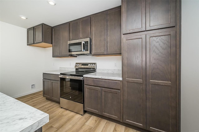 kitchen featuring appliances with stainless steel finishes, light countertops, light wood finished floors, dark brown cabinets, and baseboards