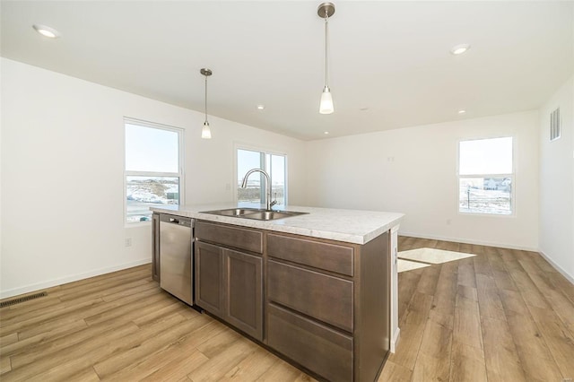 kitchen with a sink, stainless steel dishwasher, light countertops, light wood finished floors, and a kitchen island with sink