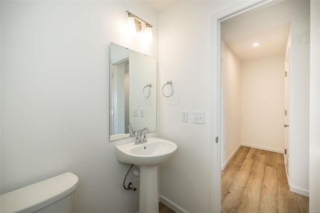 half bathroom with toilet, wood finished floors, baseboards, and a sink