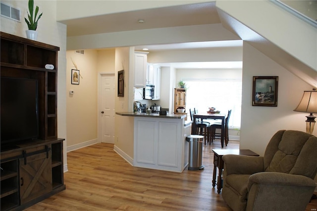10 Anemone Rd, Lake Ozark, MO 65049 - kitchen with white cabinets, stainless steel microwave, a peninsula, dark countertops, and light wood-style flooring