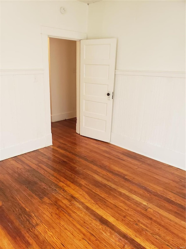 unfurnished room with wood finished floors and a wainscoted wall